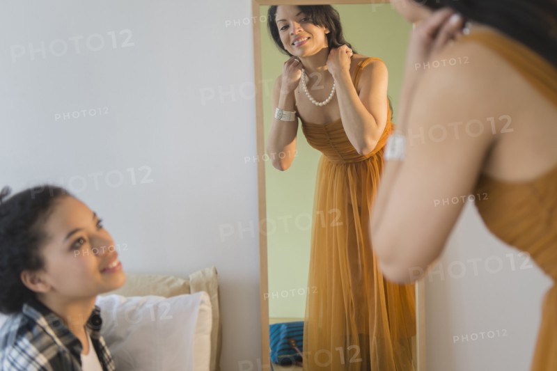Teenage girl watching mother put on evening gown