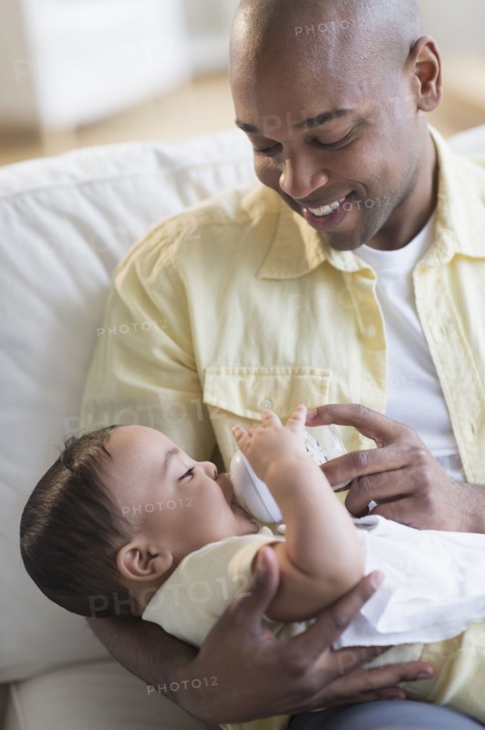 Smiling father feeding baby on sofa