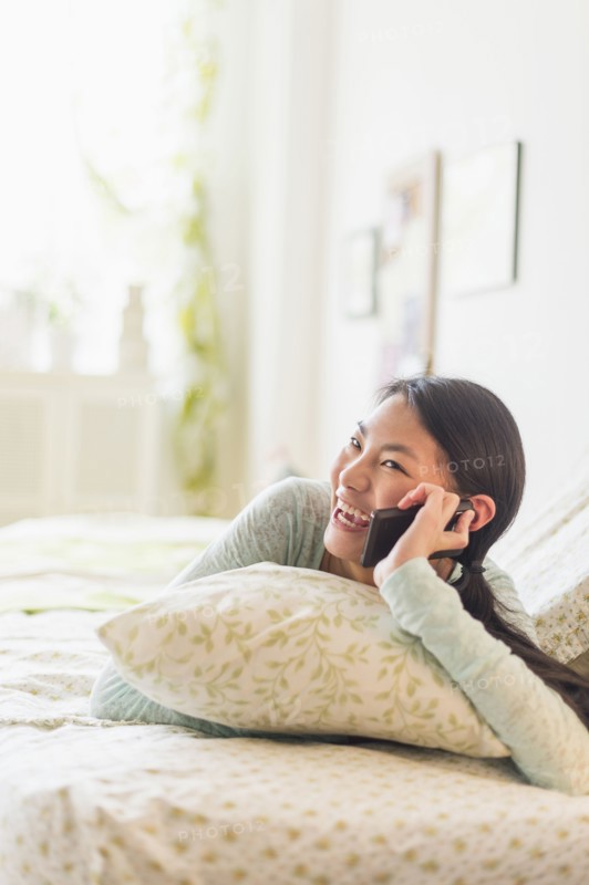 Mixed race teenage girl talking on cell phone on bed