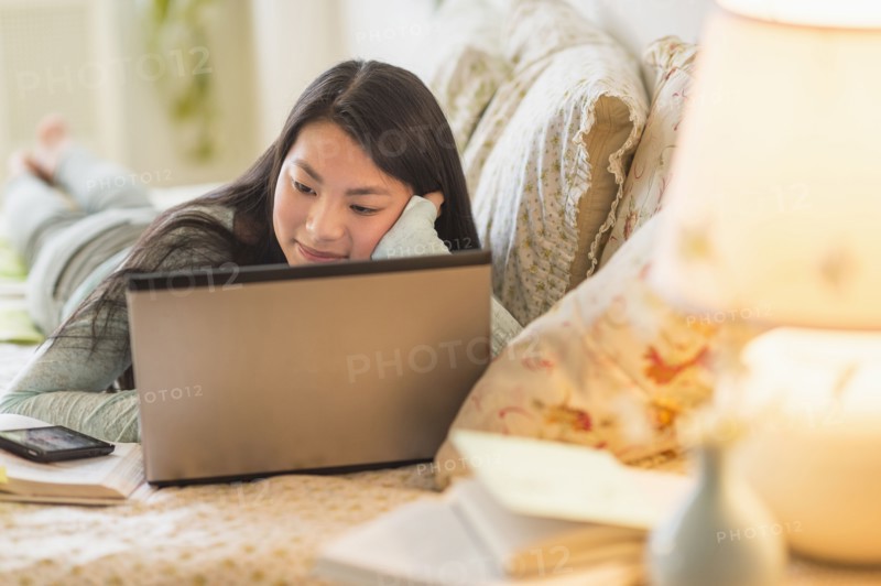 Mixed race teenage girl doing homework on bed