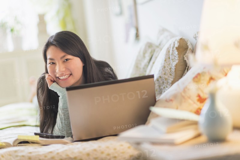 Mixed race teenage girl doing homework on bed