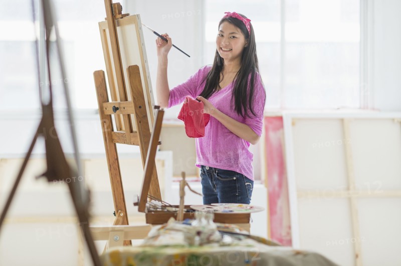 Mixed race teenage girl painting in studio