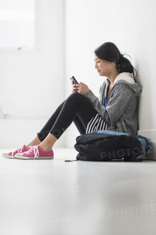 Mixed race teenage girl using cell phone in school hallway