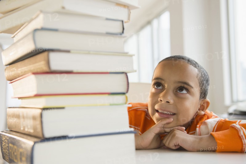 Mixed race boy looking up at stack of books
