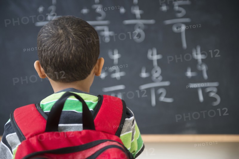 Mixed race boy doing math problems at board in class