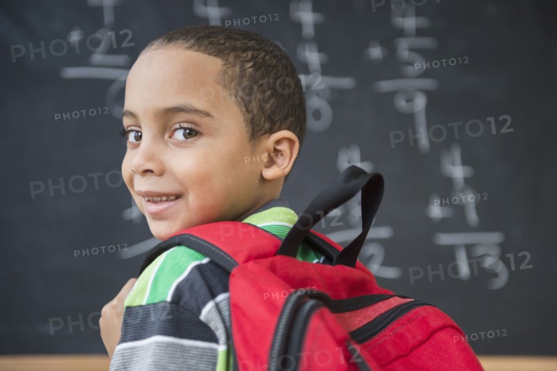 Mixed race boy doing math problems at board in class