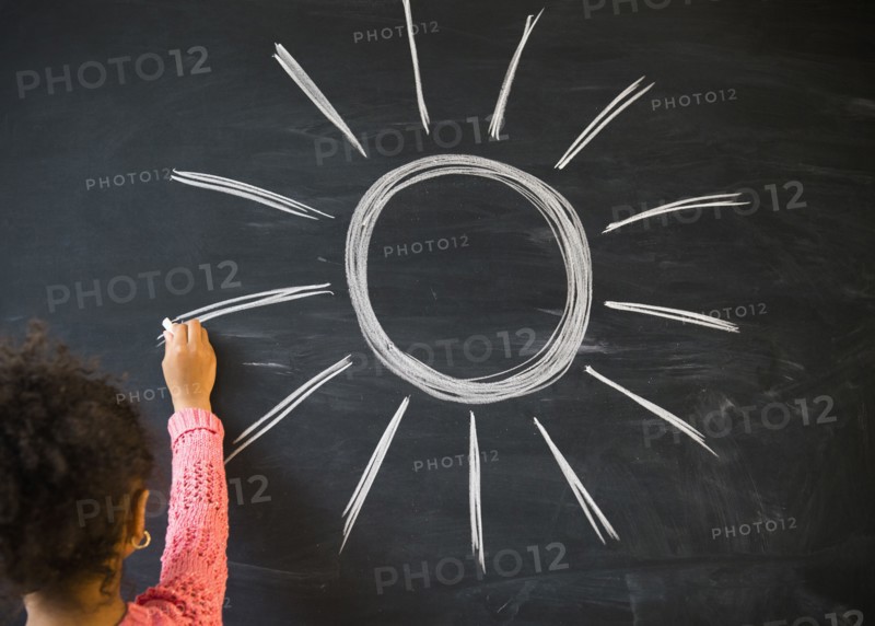 African American girl drawing sun on board in classroom