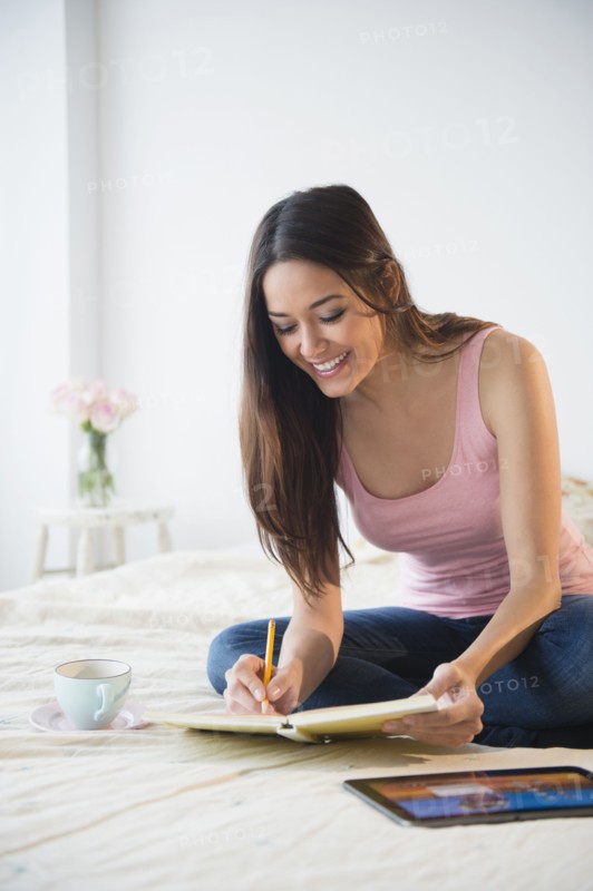 Woman taking notes with tablet computer on bed