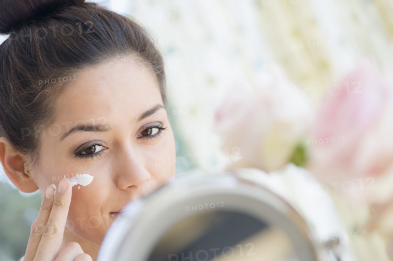 Woman applying moisturizer in mirror