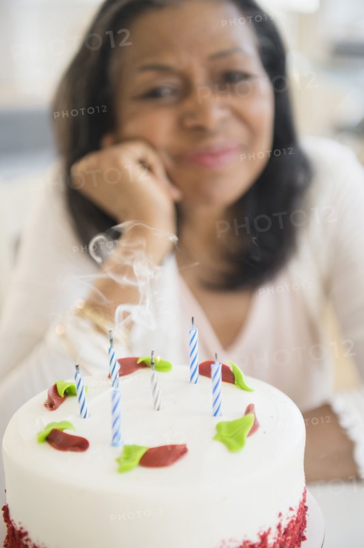 Mixed race woman blowing out birthday candles on cake