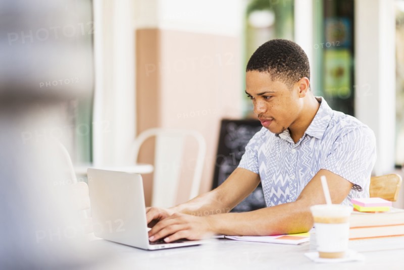 African American man using laptop at sidewalk cafe