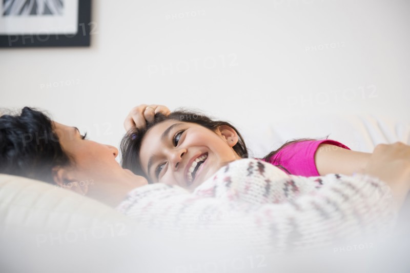 Hispanic mother and daughter relaxing together on bed