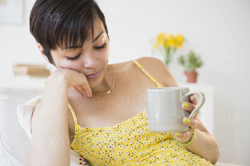 Fatigued mixed race woman drinking cup of coffee