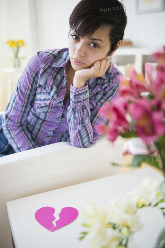 Sad mixed race woman on sofa with broken heart