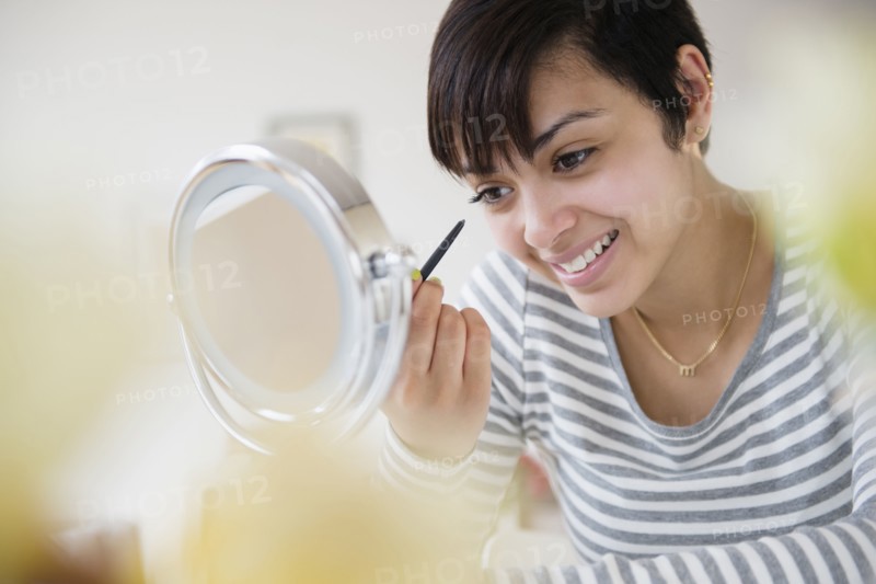 Mixed race woman applying makeup in mirror