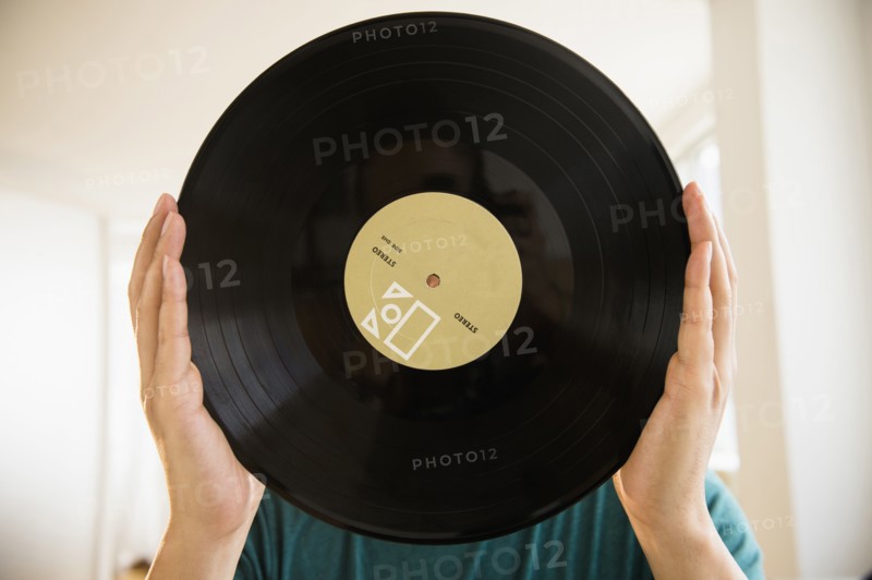 Mixed race man obscuring face with vinyl record