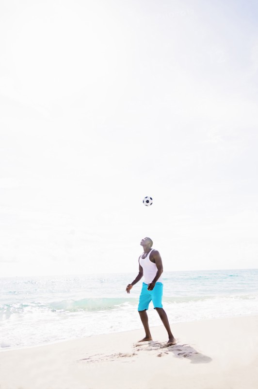 Mixed race man playing with soccer ball on beach