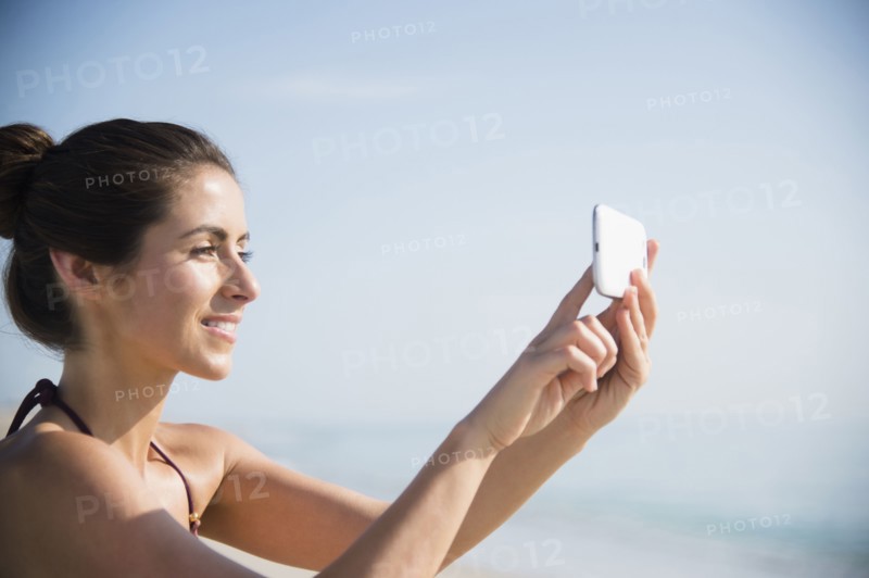 Caucasian woman taking selfie with cell phone at beach