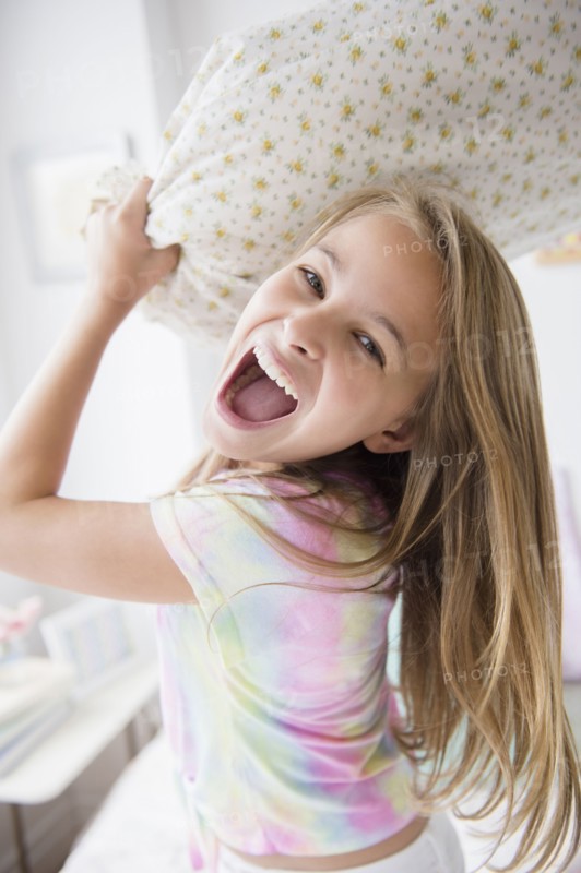 Caucasian girl having pillow fight in bedroom