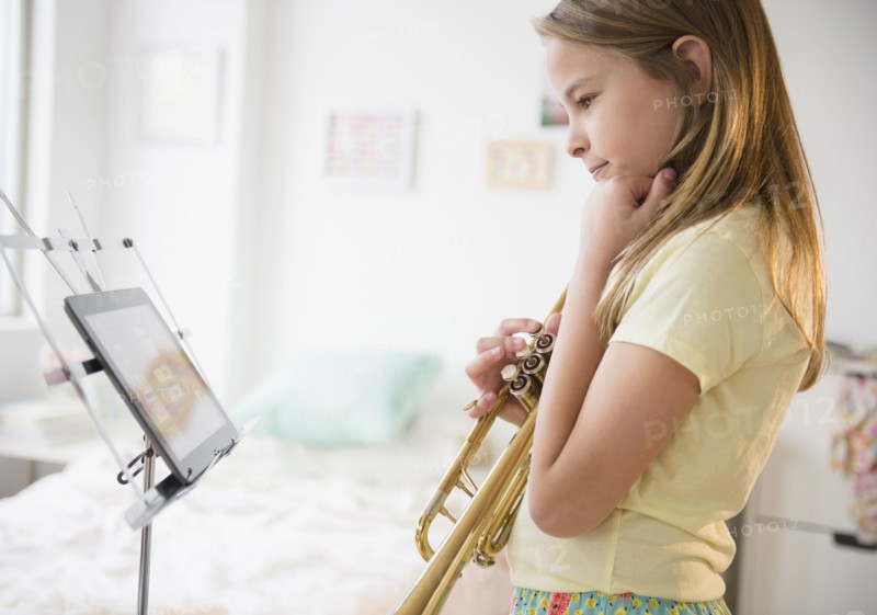 Caucasian girl practicing trumpet with digital tablet