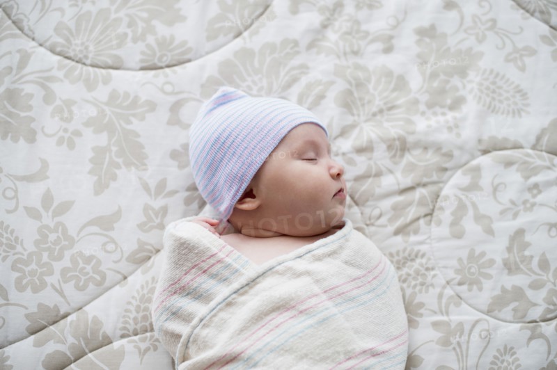 Swaddled Asian baby sleeping on bed