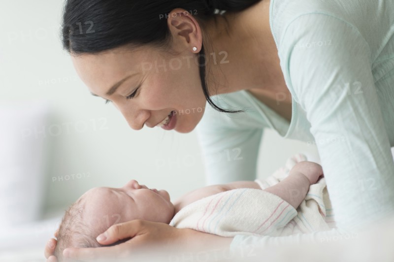 Asian mother holding baby on bed