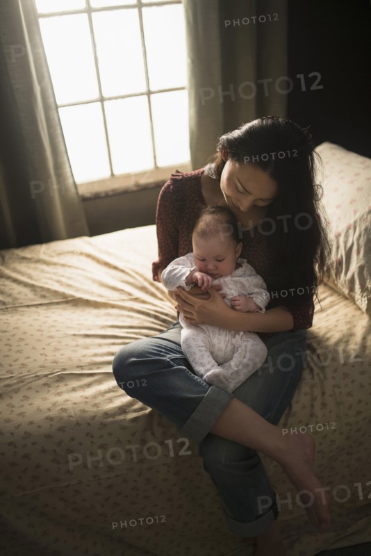 Asian mother holding baby on bed