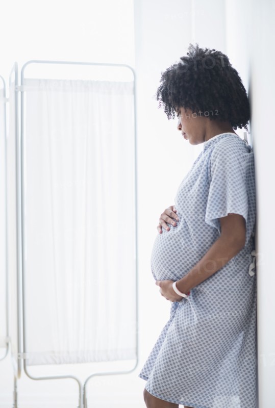 Pregnant African American mother holding stomach in hospital