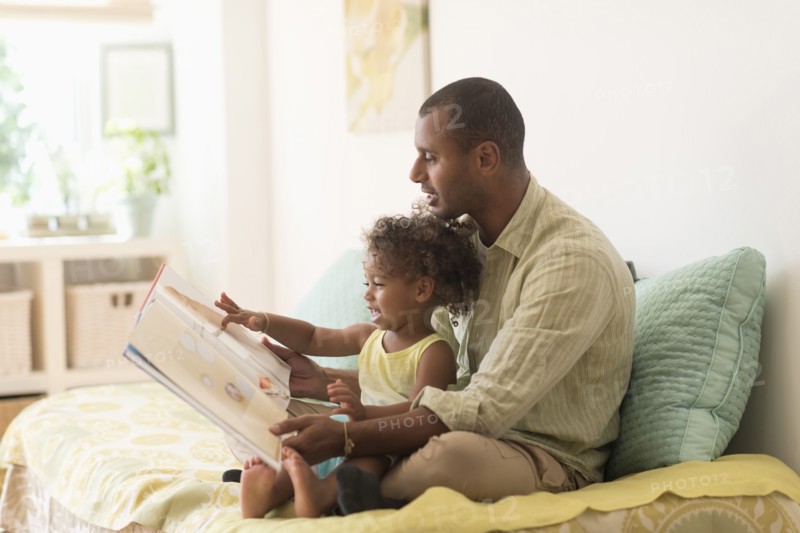 Father and daughter reading book on bed