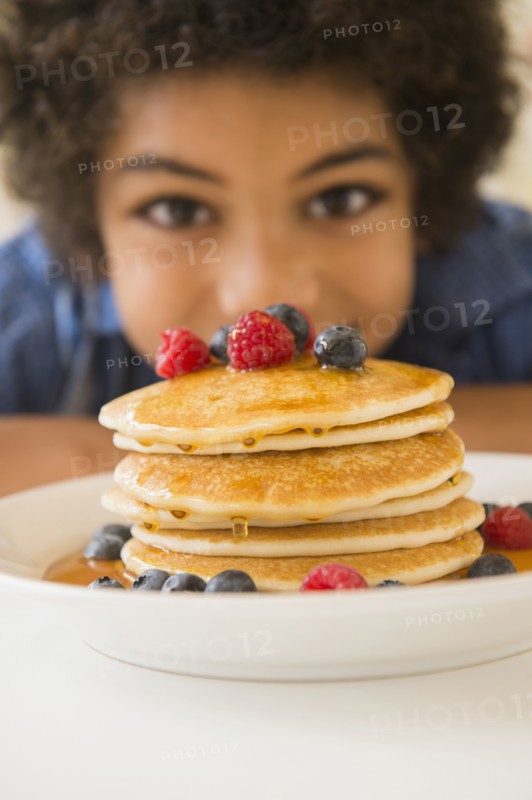 Mixed race boy admiring plate of pancakes and berries
