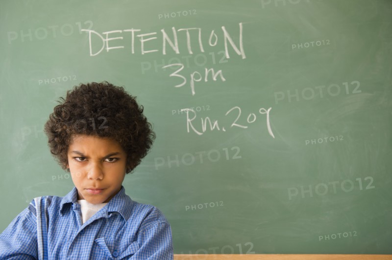 Angry mixed race boy frowning in classroom detention