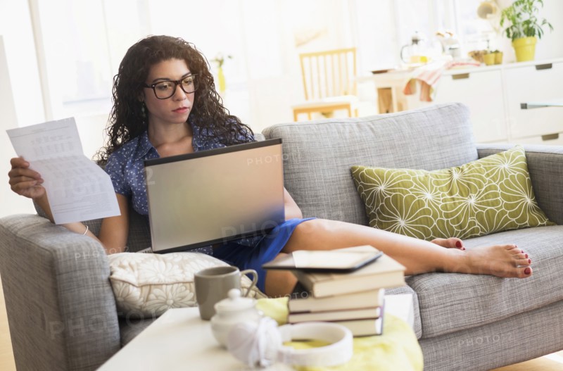 Mixed race woman paying bills on laptop on sofa
