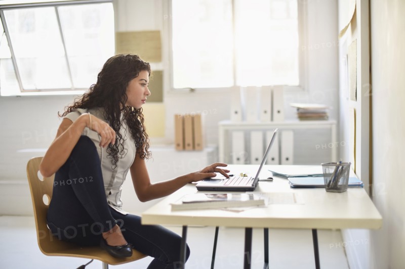 Mixed race businesswoman working on laptop at desk in office