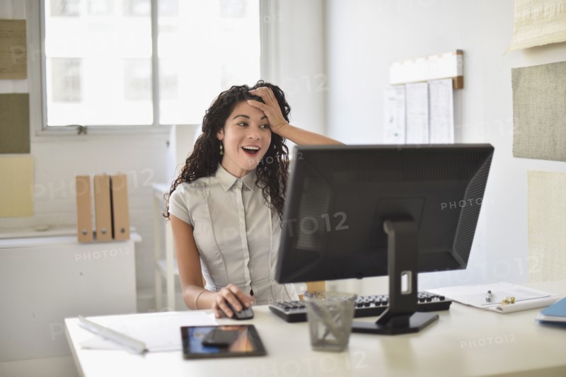 Mixed race businesswoman gasping at computer at desk in office