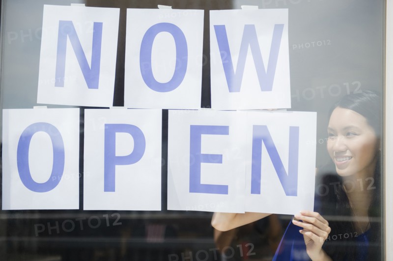 Woman hanging now open sign in store window