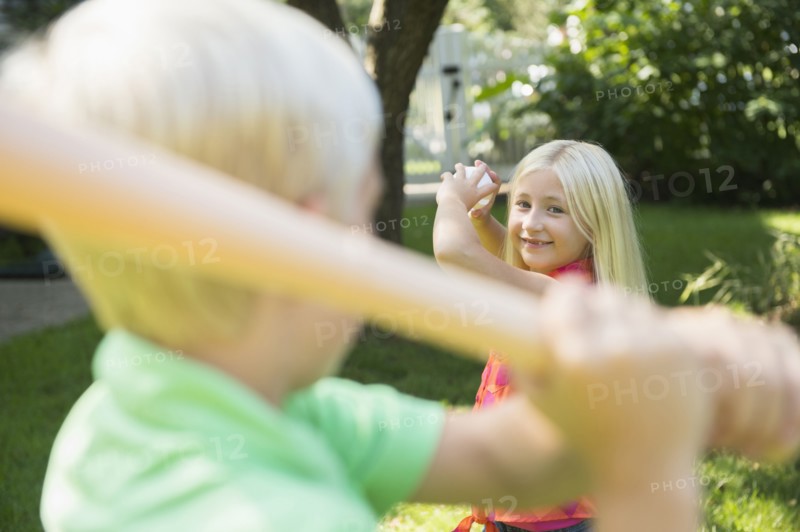 Caucasian children playing baseball in backyard