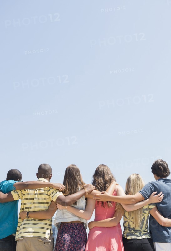 Rear view of teenagers hugging under blue sky