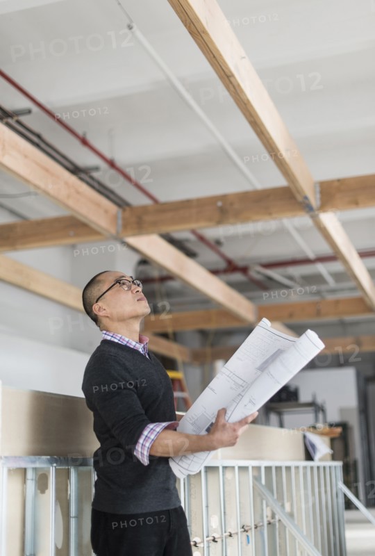 Korean architect holding blueprints and examining ceiling