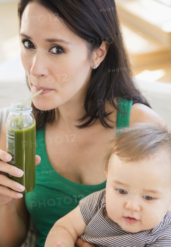 Close up of mixed race mother holding baby and drinking green juice