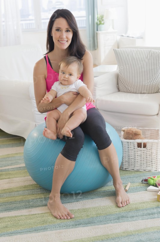 Mixed race mother holding baby on fitness ball