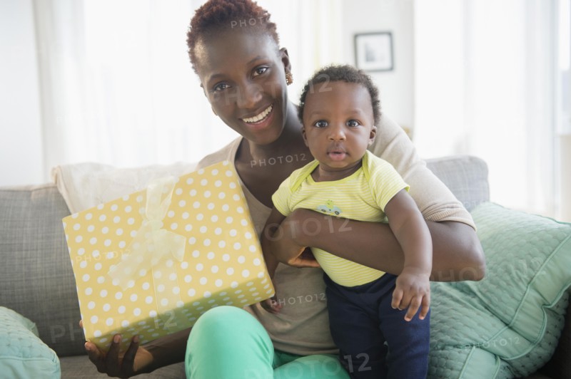 Black mother and son holding gift on sofa