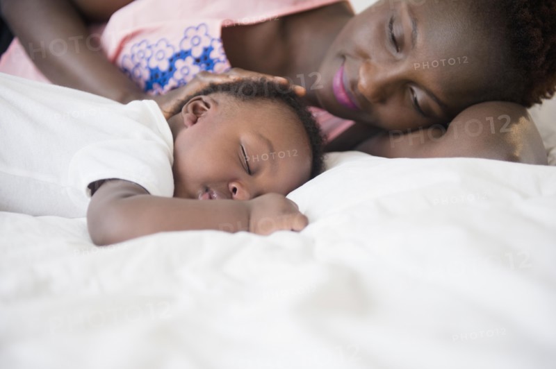 Black mother admiring sleeping son on bed