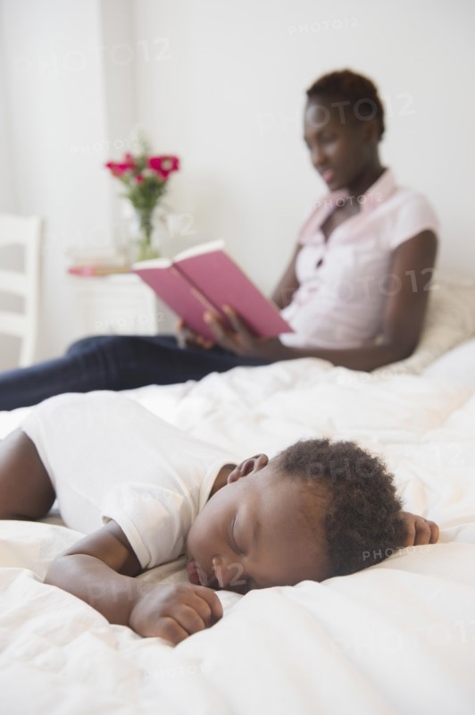 Black mother reading near sleeping baby boy