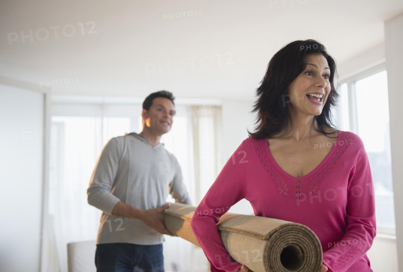 Couple carrying roll of carpet in living room