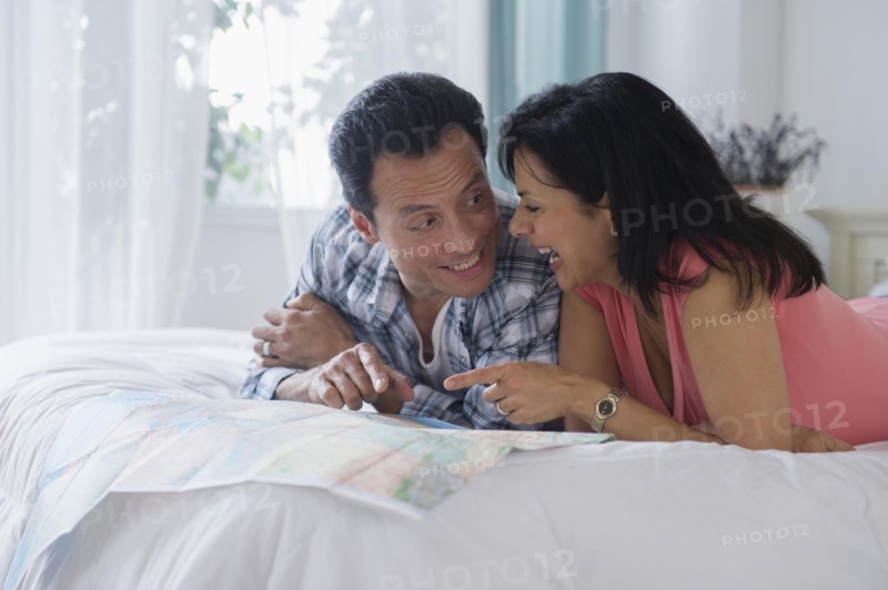 Couple reading map on bed