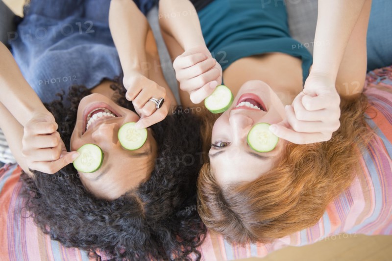 Women holding cucumber slices over eyes