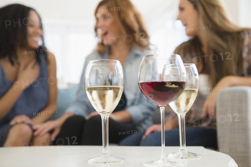 Women drinking wine and talking on sofa in living room