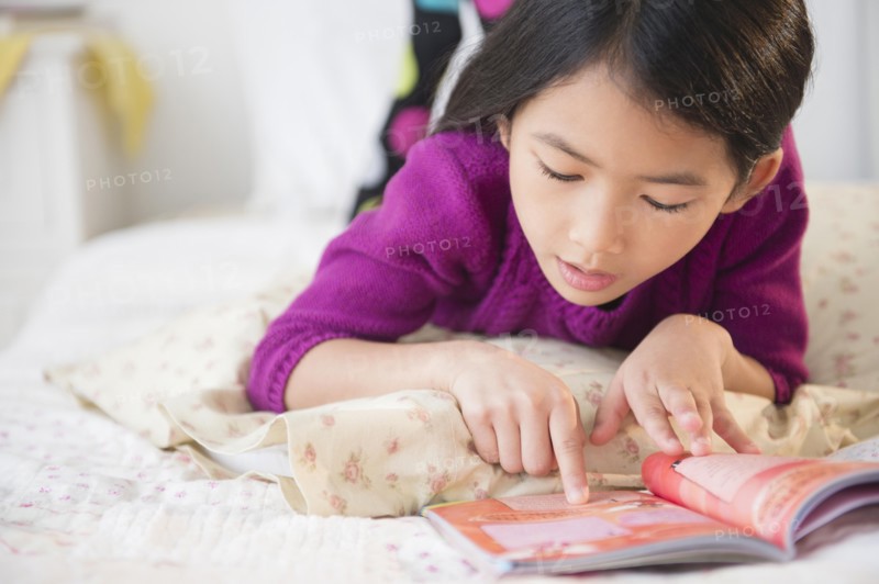 Close up of Vietnamese girl reading book on bed
