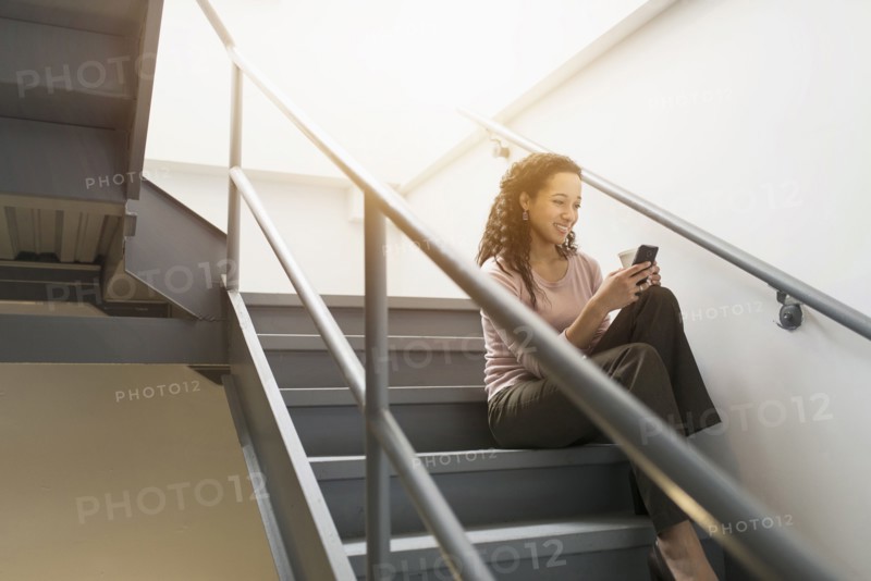 Low angle view of mixed race businesswoman using cell phone on staircase