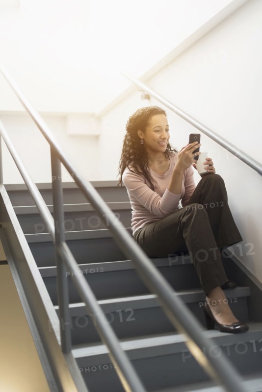 Low angle view of mixed race businesswoman using cell phone on staircase